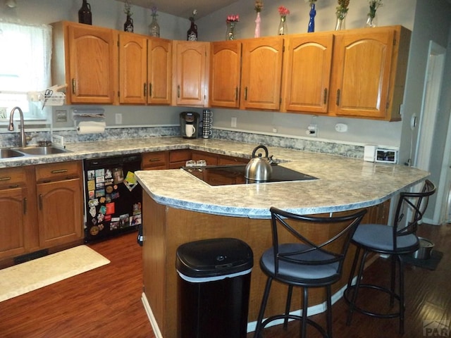 kitchen with dark wood-style floors, light countertops, black appliances, a breakfast bar area, and a sink