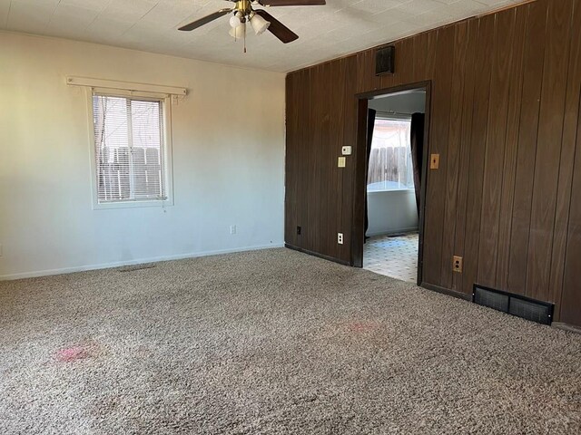 spare room featuring plenty of natural light, visible vents, wood walls, and carpet flooring