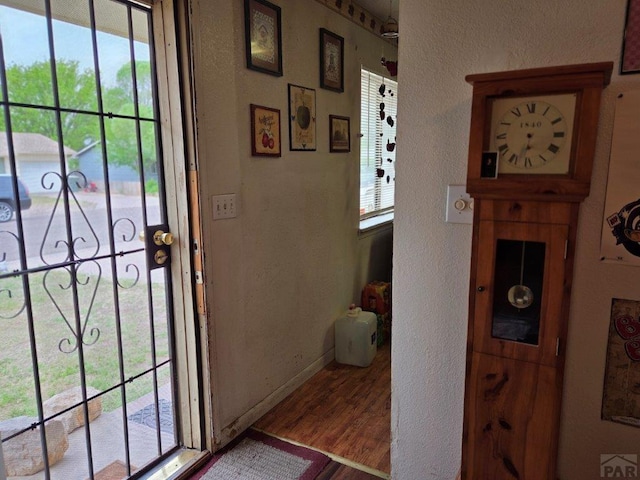 doorway to outside featuring baseboards, wood finished floors, and a textured wall