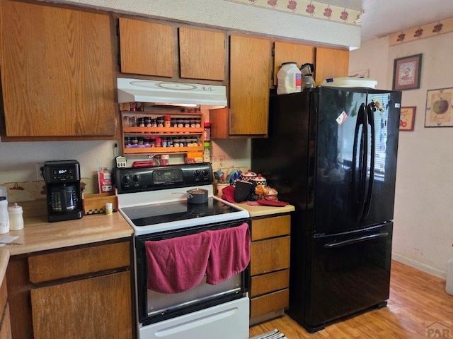 kitchen with under cabinet range hood, light countertops, freestanding refrigerator, and electric stove