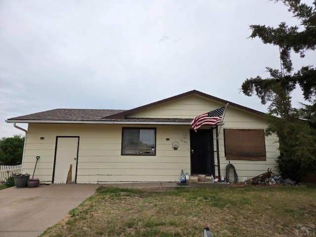 view of front of property with a front yard, a shingled roof, and fence