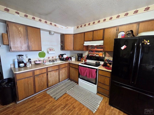 kitchen with freestanding refrigerator, a textured ceiling, under cabinet range hood, white electric stove, and a sink