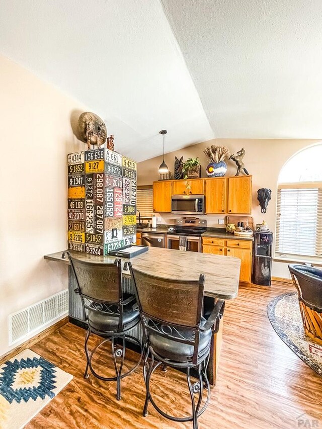 dining room featuring lofted ceiling, a textured ceiling, visible vents, baseboards, and light wood-type flooring