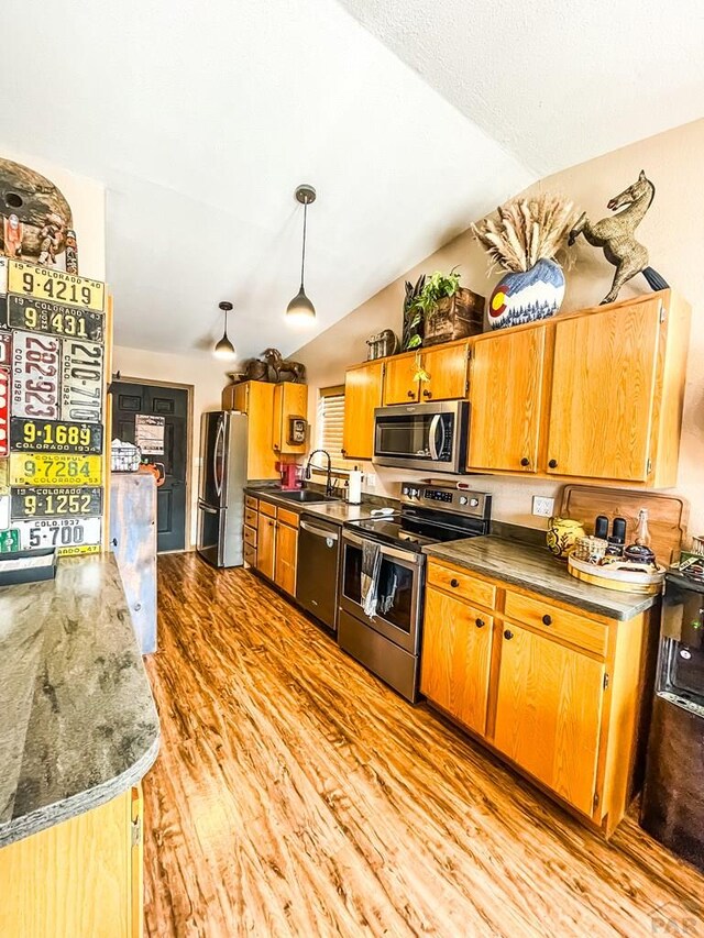 kitchen with light wood-style flooring, appliances with stainless steel finishes, brown cabinetry, vaulted ceiling, and a sink