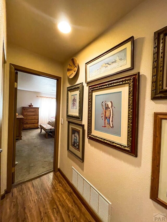 hallway with baseboards, visible vents, and dark wood finished floors