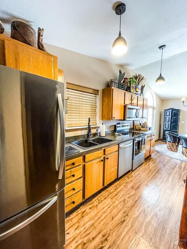 kitchen featuring stainless steel appliances, a sink, light wood-type flooring, dark countertops, and pendant lighting