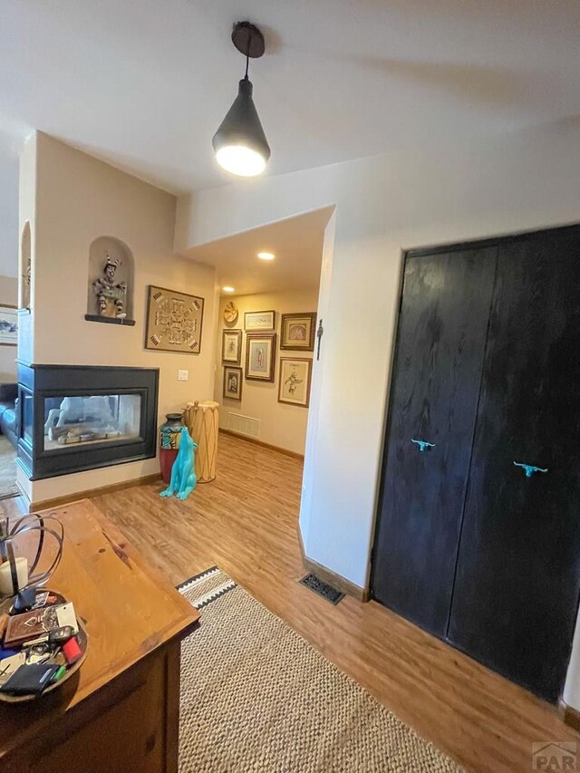 living area featuring visible vents, baseboards, light wood finished floors, and a multi sided fireplace