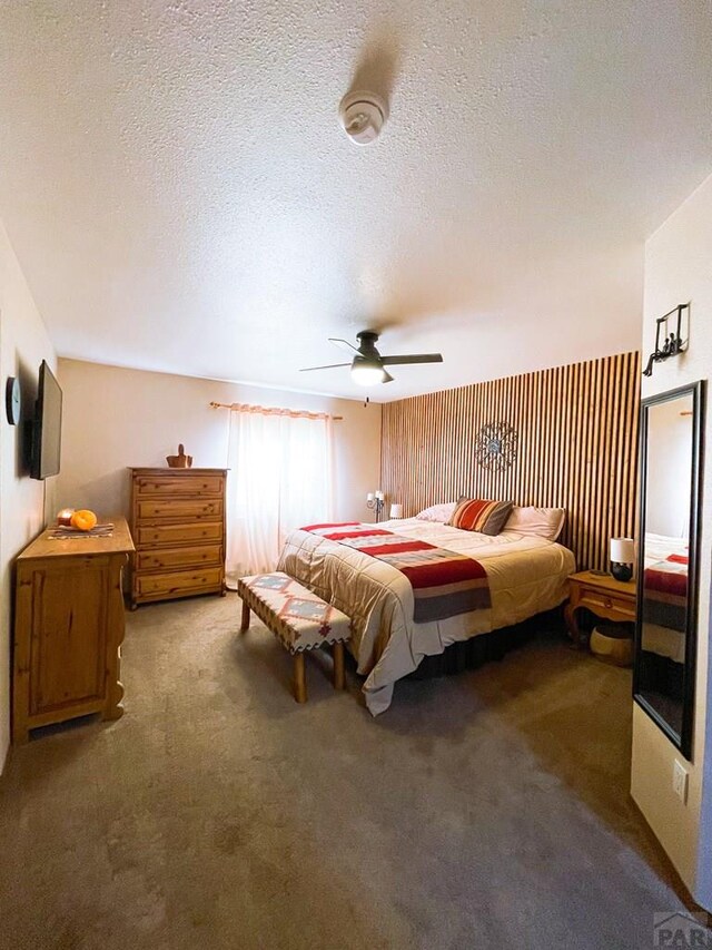 bedroom with a textured ceiling, dark carpet, and a ceiling fan