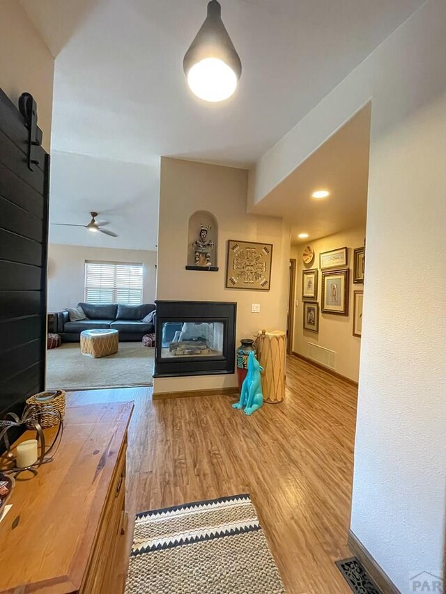 living area featuring visible vents, a ceiling fan, a multi sided fireplace, light wood-type flooring, and baseboards