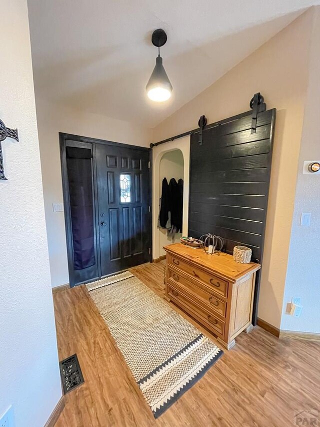 foyer featuring a barn door, baseboards, visible vents, vaulted ceiling, and light wood-type flooring