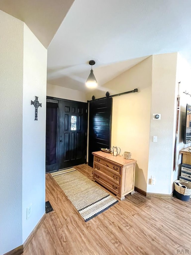 foyer entrance featuring lofted ceiling, a barn door, wood finished floors, and baseboards