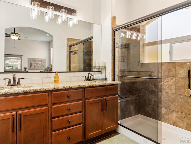 bathroom with a ceiling fan, a sink, a shower stall, and double vanity