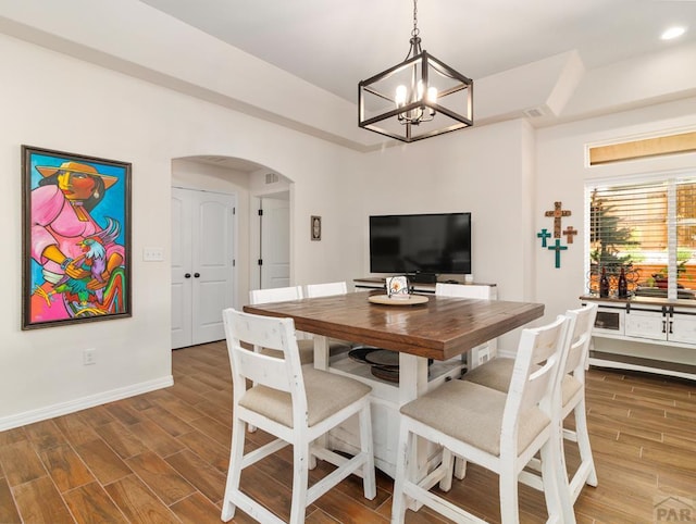 dining area featuring wood tiled floor, arched walkways, a chandelier, and baseboards