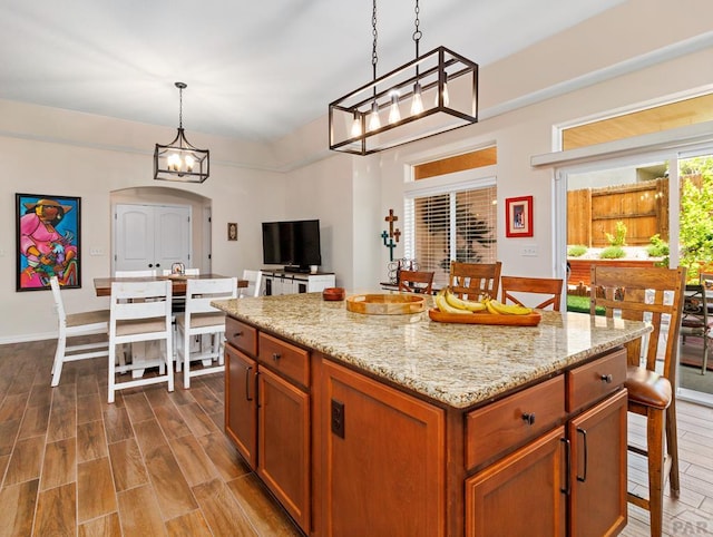 kitchen featuring arched walkways, a kitchen island, brown cabinets, decorative light fixtures, and wood tiled floor