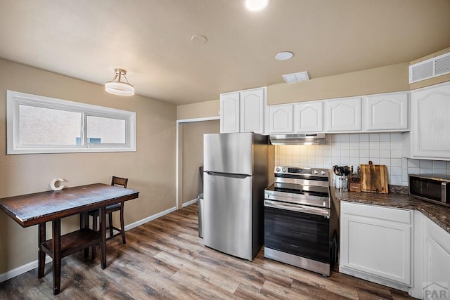 kitchen with stainless steel appliances, under cabinet range hood, dark countertops, white cabinetry, and tasteful backsplash