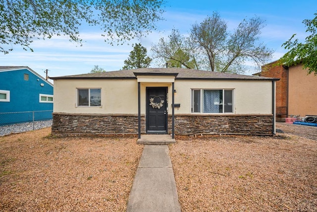 view of front of home featuring stone siding, stucco siding, fence, and roof with shingles