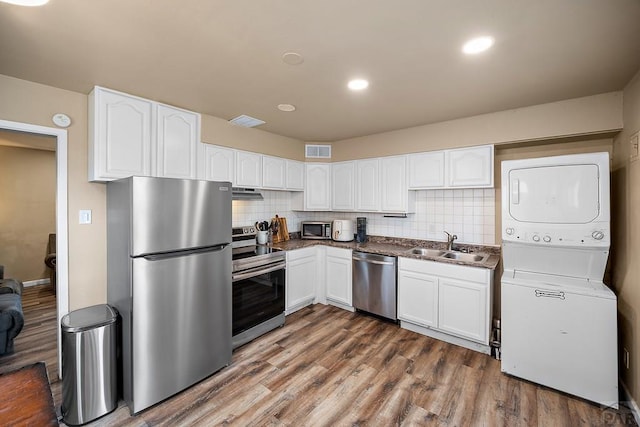 kitchen with appliances with stainless steel finishes, estacked washer and dryer, white cabinetry, dark wood-type flooring, and a sink