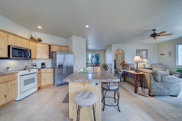 kitchen featuring a center island, open shelves, appliances with stainless steel finishes, a breakfast bar, and light brown cabinetry