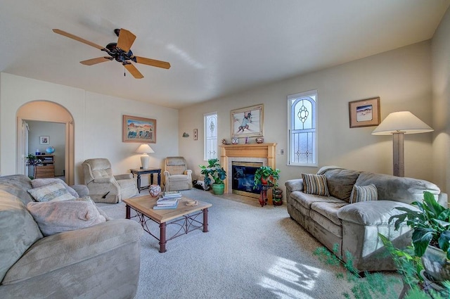 living room featuring carpet floors, a ceiling fan, arched walkways, and a fireplace with flush hearth