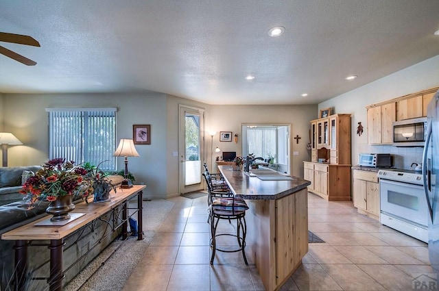 kitchen with stainless steel microwave, dark countertops, white range with electric stovetop, a sink, and light brown cabinetry