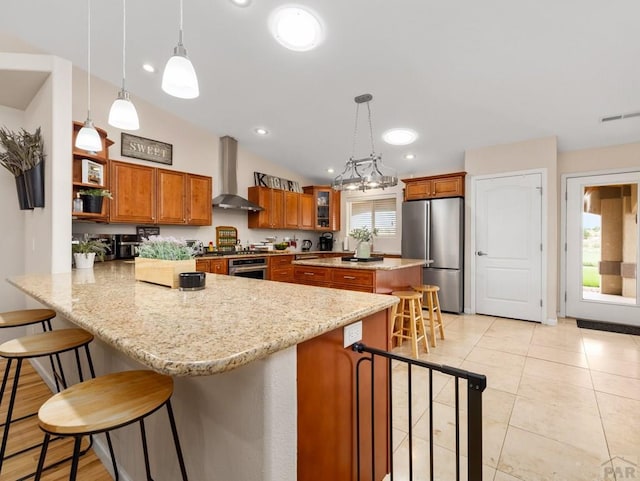 kitchen featuring stainless steel appliances, a peninsula, a breakfast bar, wall chimney range hood, and pendant lighting