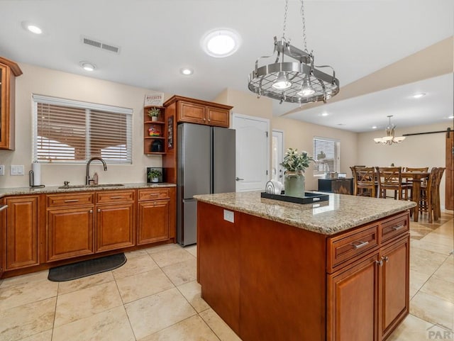 kitchen with brown cabinets, a center island, hanging light fixtures, freestanding refrigerator, and a sink