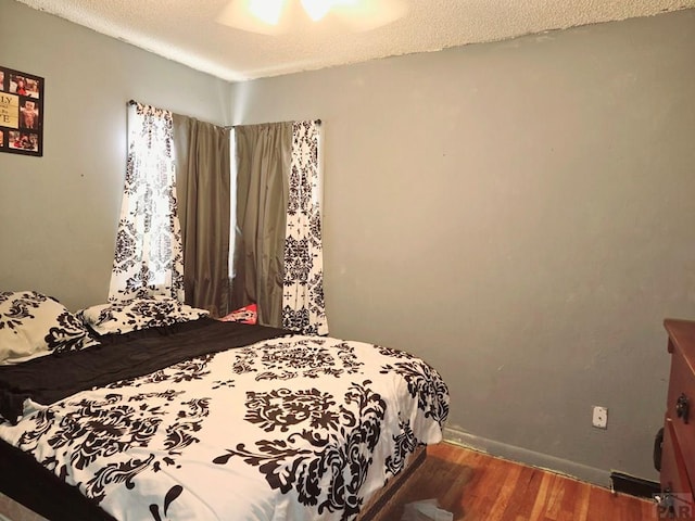 bedroom with a textured ceiling, baseboards, and wood finished floors