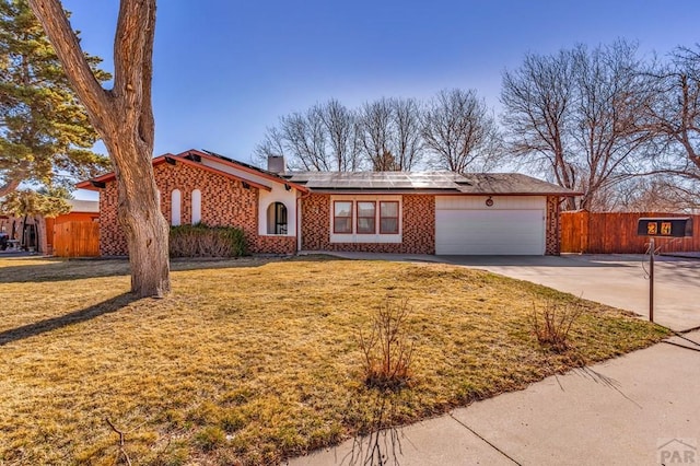 view of front of property with solar panels, fence, concrete driveway, a front yard, and a garage