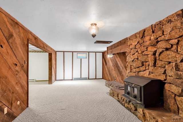 interior space featuring a wood stove, wooden walls, carpet, and baseboard heating