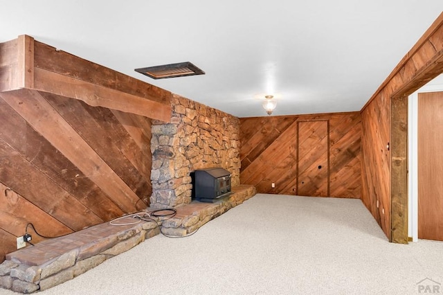 below grade area featuring a wood stove, carpet flooring, and wood walls