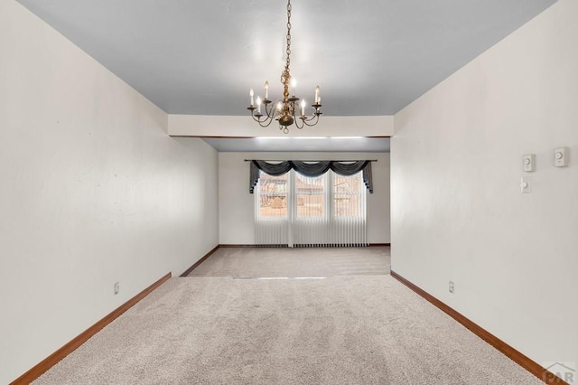 carpeted empty room featuring a notable chandelier and baseboards