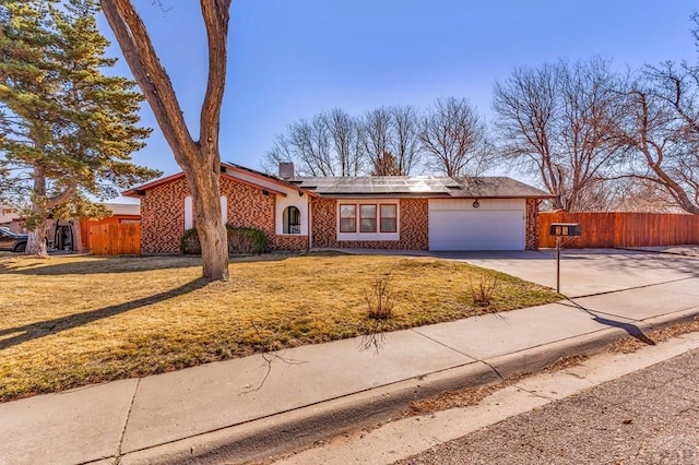 ranch-style home featuring a front yard, fence, driveway, an attached garage, and roof mounted solar panels