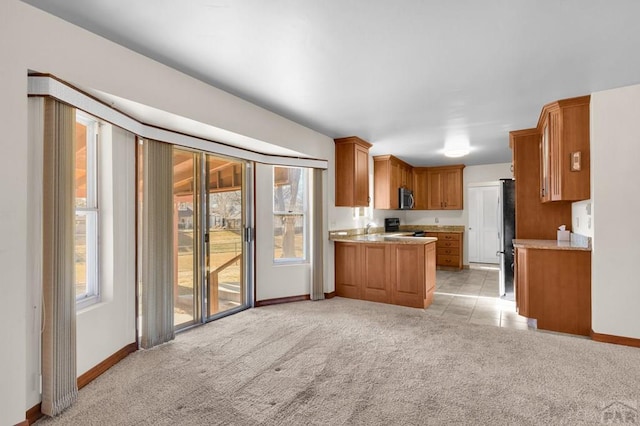 kitchen with baseboards, light countertops, light carpet, brown cabinets, and stainless steel appliances