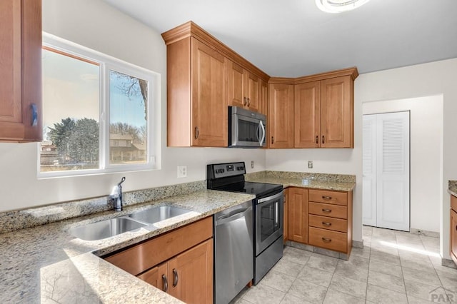 kitchen with light stone counters, light tile patterned floors, brown cabinetry, stainless steel appliances, and a sink