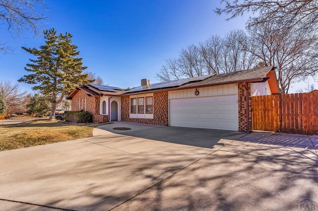 view of front of house featuring fence, concrete driveway, a garage, brick siding, and solar panels