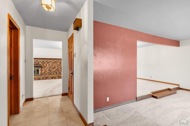 hall with light tile patterned floors, beamed ceiling, baseboards, and light colored carpet