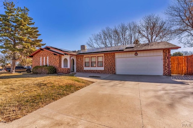 view of front of property featuring fence, driveway, an attached garage, brick siding, and roof mounted solar panels