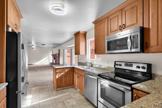 kitchen with a sink, a peninsula, light stone counters, and stainless steel appliances