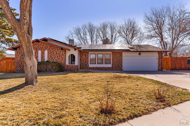 view of front of property with fence, a front lawn, a garage, brick siding, and roof mounted solar panels