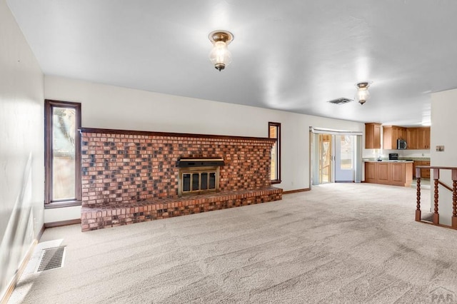 unfurnished living room with light colored carpet, a fireplace, visible vents, and baseboards