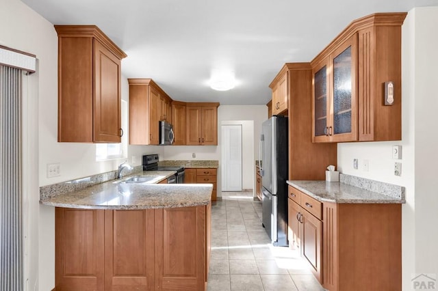 kitchen featuring brown cabinets, a sink, light stone counters, appliances with stainless steel finishes, and a peninsula