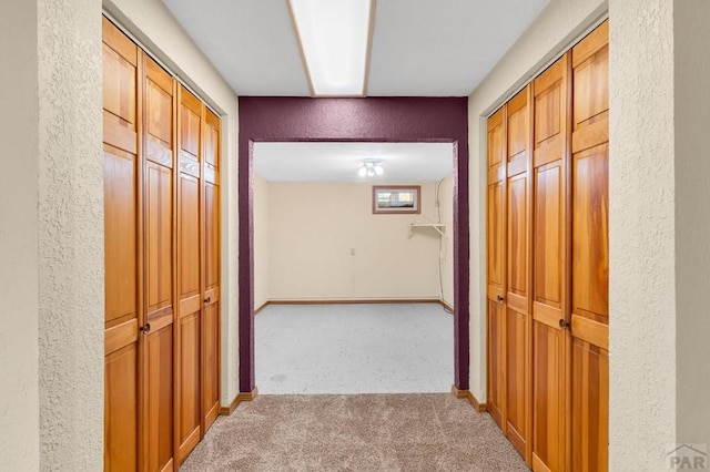 hall featuring light colored carpet, baseboards, and a textured wall