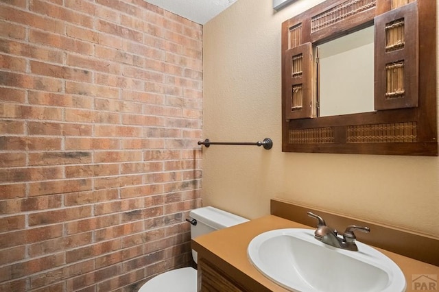 half bath with brick wall, vanity, and toilet