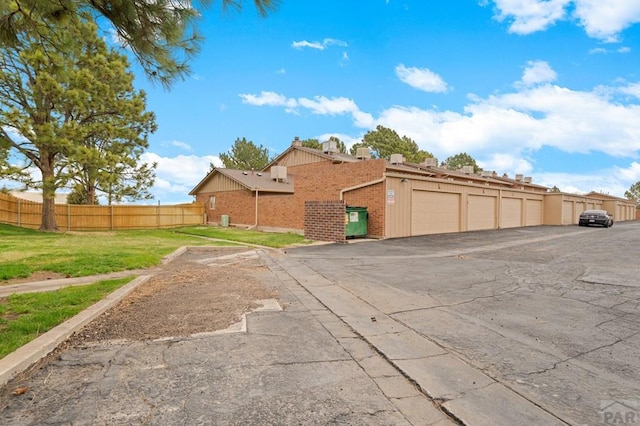 view of side of home with brick siding, a lawn, fence, and community garages