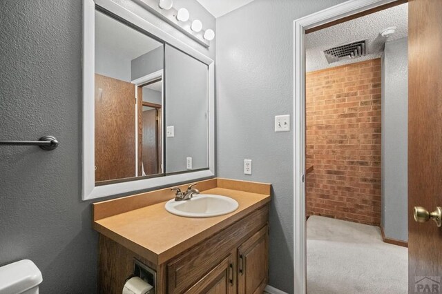 bathroom with visible vents, a textured wall, vanity, and toilet