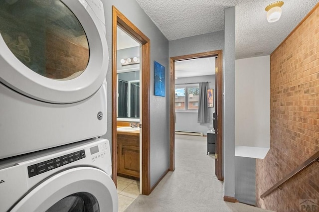 laundry room featuring a baseboard heating unit, stacked washer / dryer, a sink, a textured ceiling, and laundry area