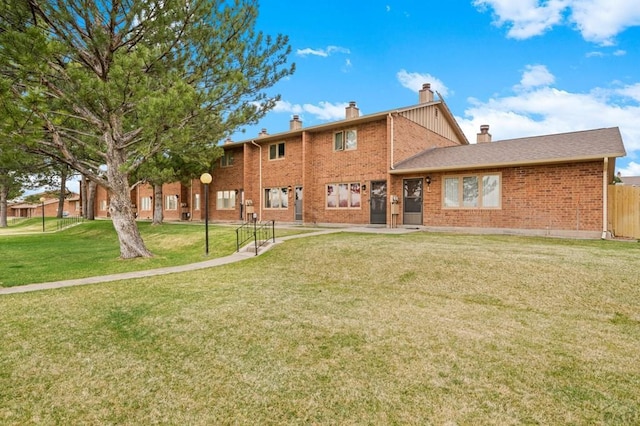 back of property featuring a yard, brick siding, a chimney, and fence