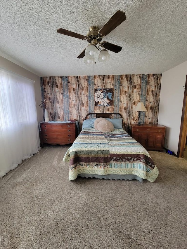 bedroom with a textured ceiling, wood walls, a ceiling fan, and carpet floors