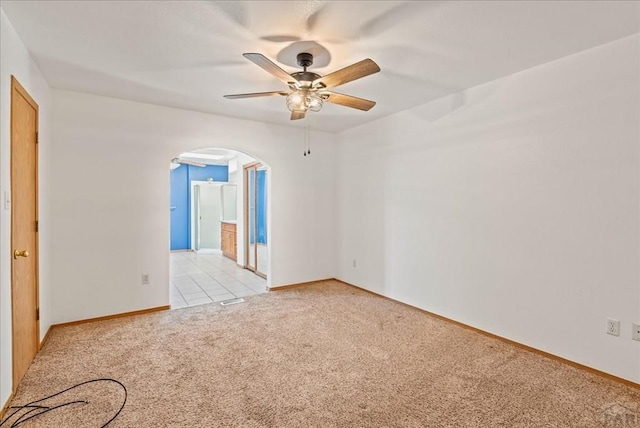 unfurnished room featuring arched walkways, light tile patterned floors, light carpet, ceiling fan, and baseboards