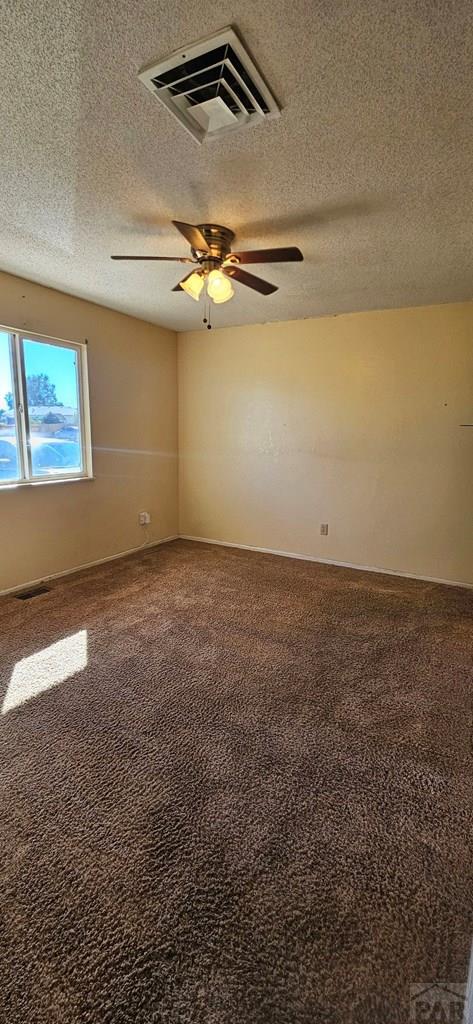 carpeted spare room featuring ceiling fan, visible vents, and a textured ceiling